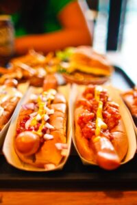 Close-up of various hotdogs with toppings on a wooden table, ideal for fast food themes.